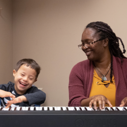 a young boy and an older woman sit at a piano keyboard
