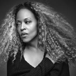 Portrait of Black woman with long, wavy hair looking away from the camera, wearing a black shirt.