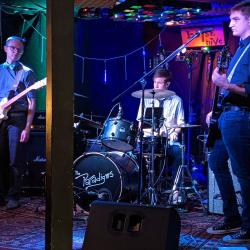 Three men who are members of a band stand onstage ready to perform