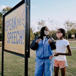 An woman and a girl read a bill board in a park.