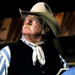 A man in a coboy hat sitting with a book on his lap.