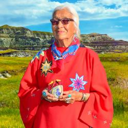 A woamn in traditional dress stands with a mountain in the background.