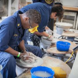 Seated man looks down at clay on a round surface while he works it with his hands