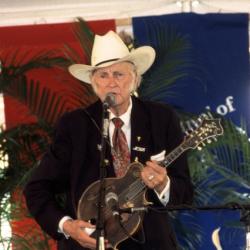 Man in cowboy hat playing a mandolin on stage.