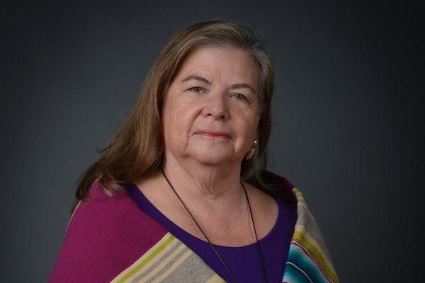 A woman with brown and grey hair is wrapped in a multicolored striped shawl