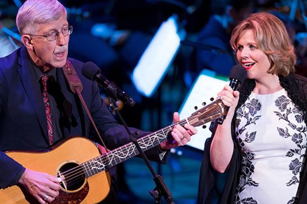 An older man playing a guitar next to a woman singing