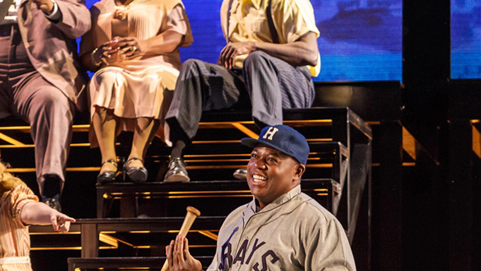 Man in baseball uniform holding a bat on stage. 