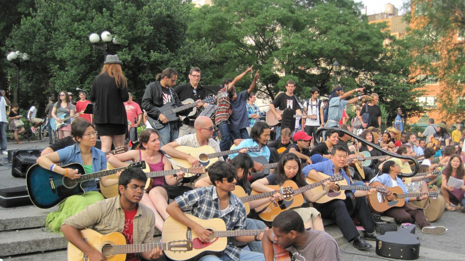 group of guitar players sitting in a park