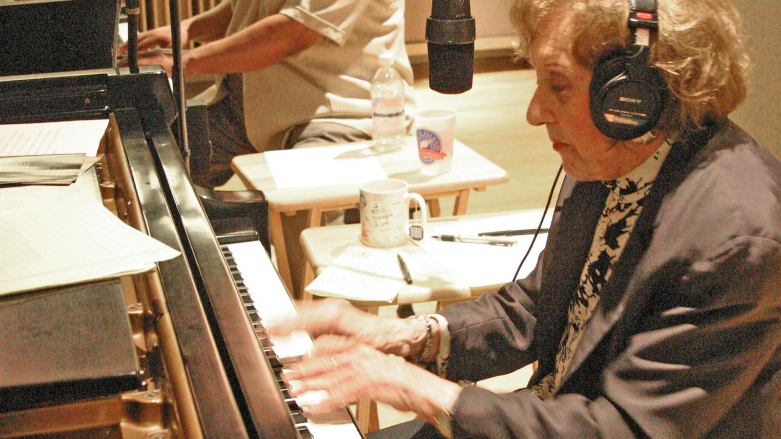 Woman wearing headphones playing piano with African-American man behind her playing piano.