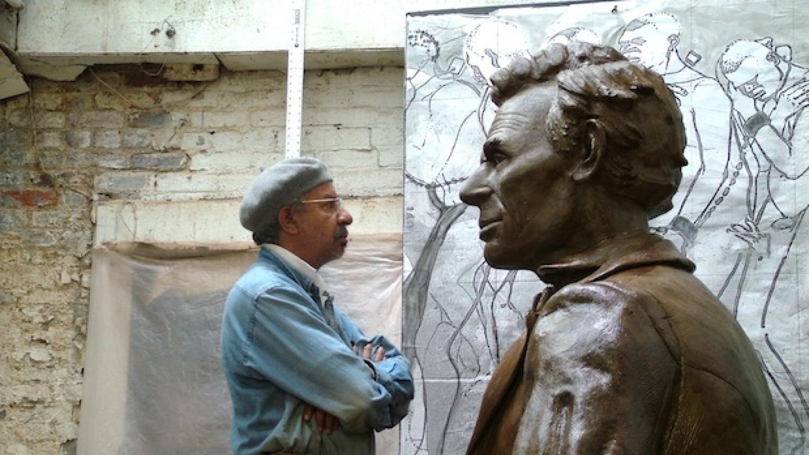 an older African American man stands face to face with a very large size bronze sculpture of Abraham Lincoln