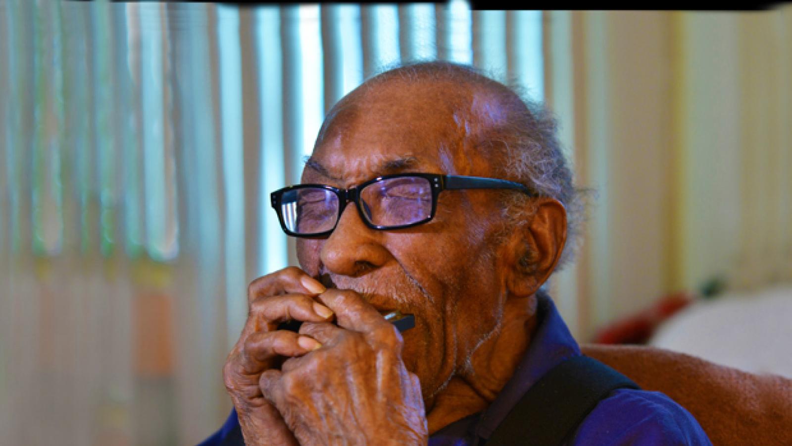 A man plays the harmonica with his eyes closed.