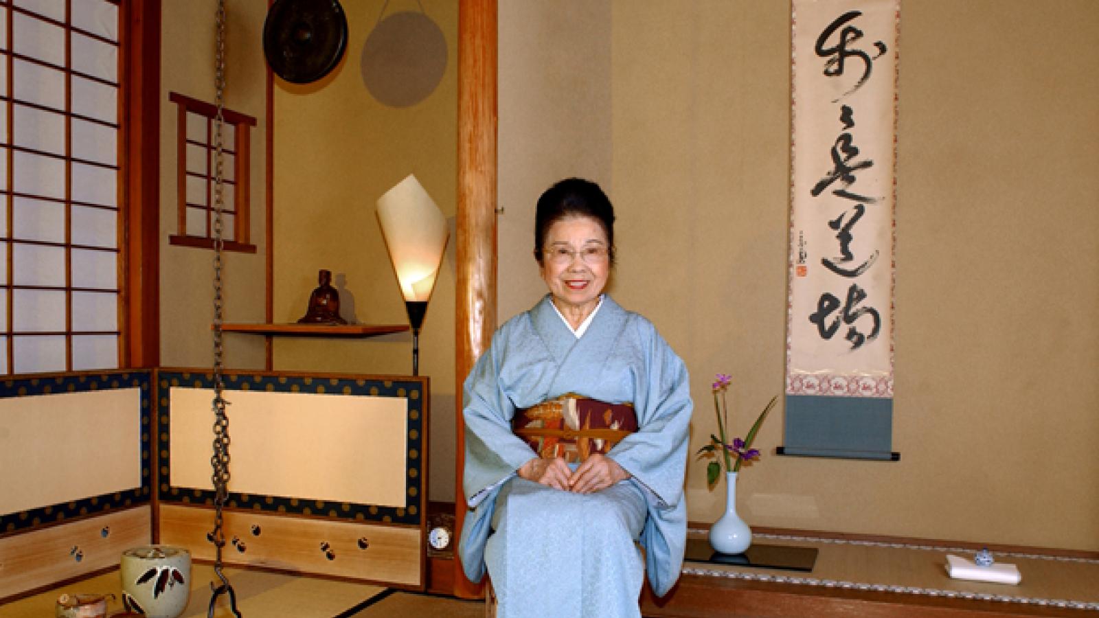 A woman in traditional Japanese clothing sits next to tea ware.