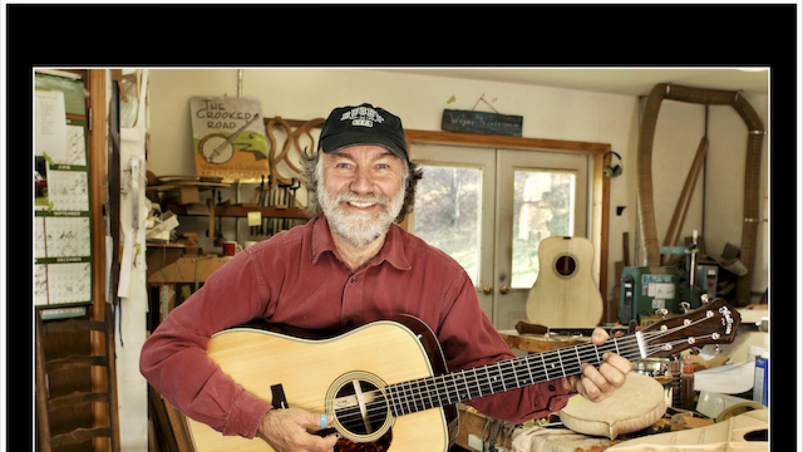 a man holding a guitar in his luthier's workshop