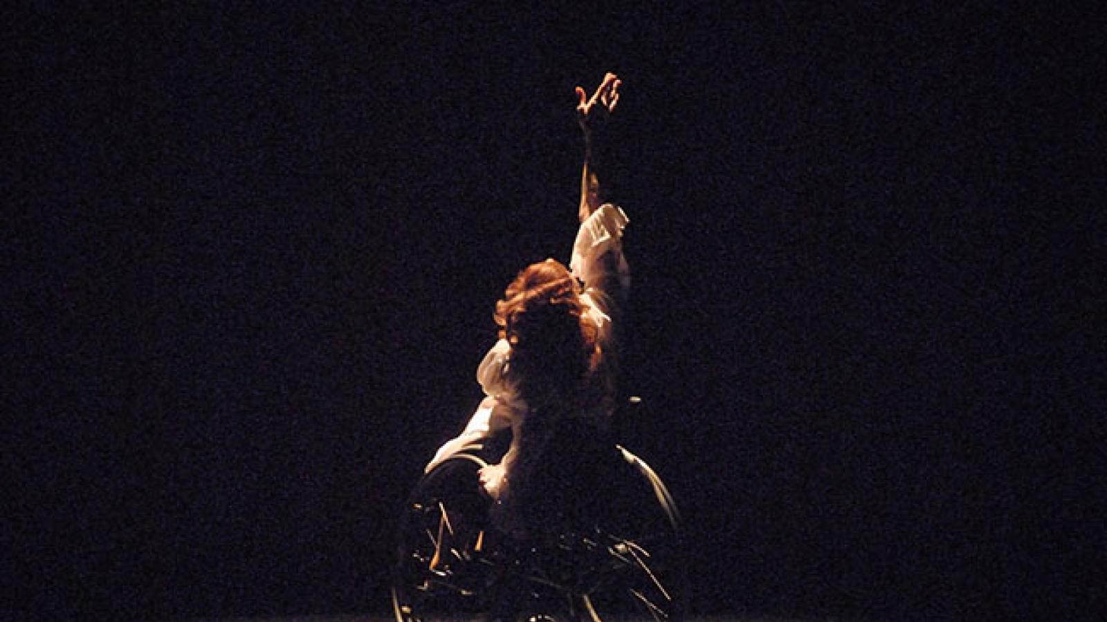 Mary Verdi-Fletcher A dancer in a wheelchair lifts one hand upward as she performs onstage