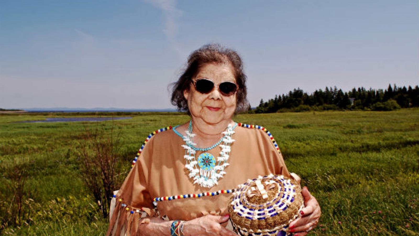 Woman in traditional dress holding a woven basket and standing in a large field.