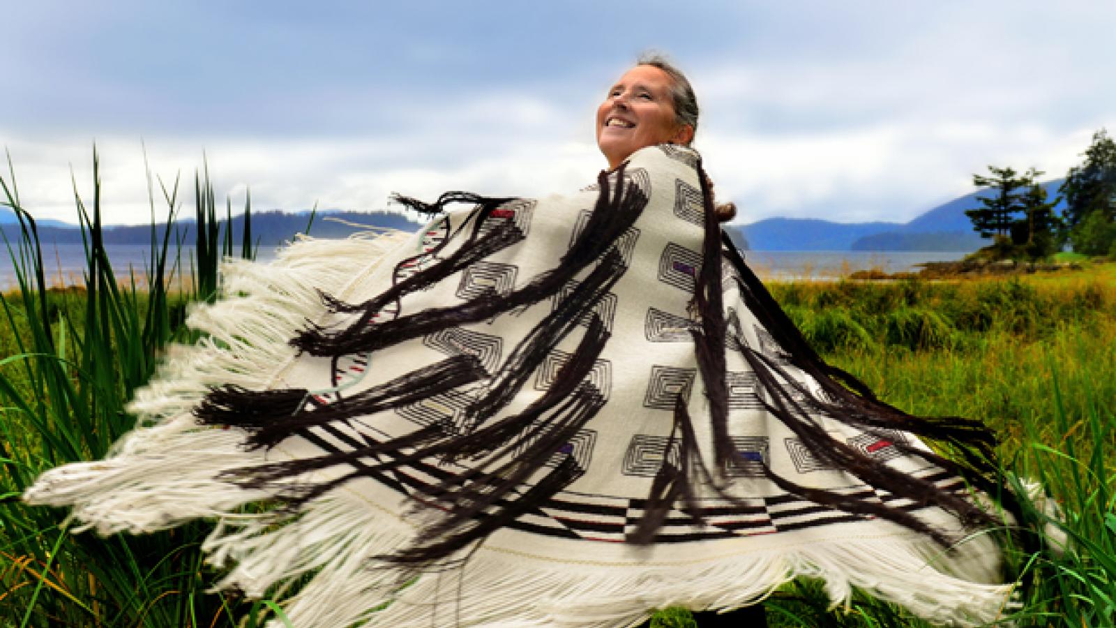 A woman stands in a field twirling while wearing a black and white woven robe.