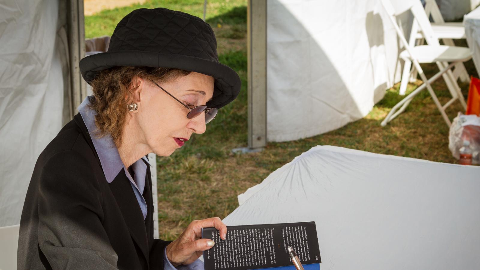 Joyce Carol Oates sitting down and signing her book for a reader.