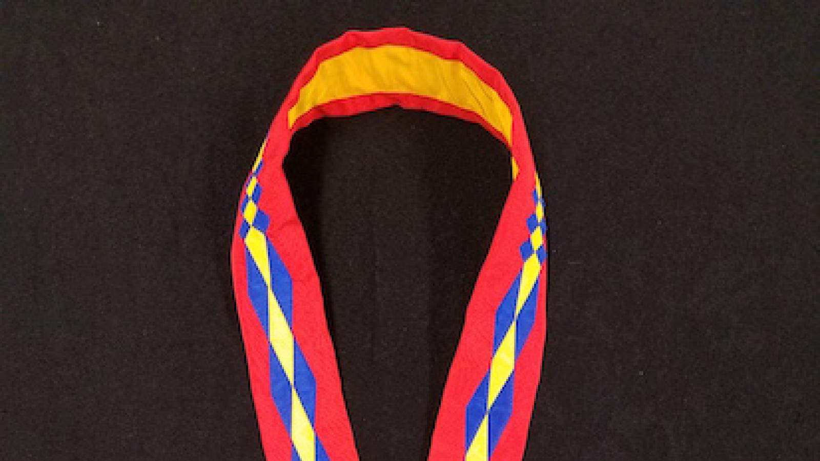 circular medal with filigree heart in cut-out center hung from red, blue and yellow ribbon in Osage traiditional patter