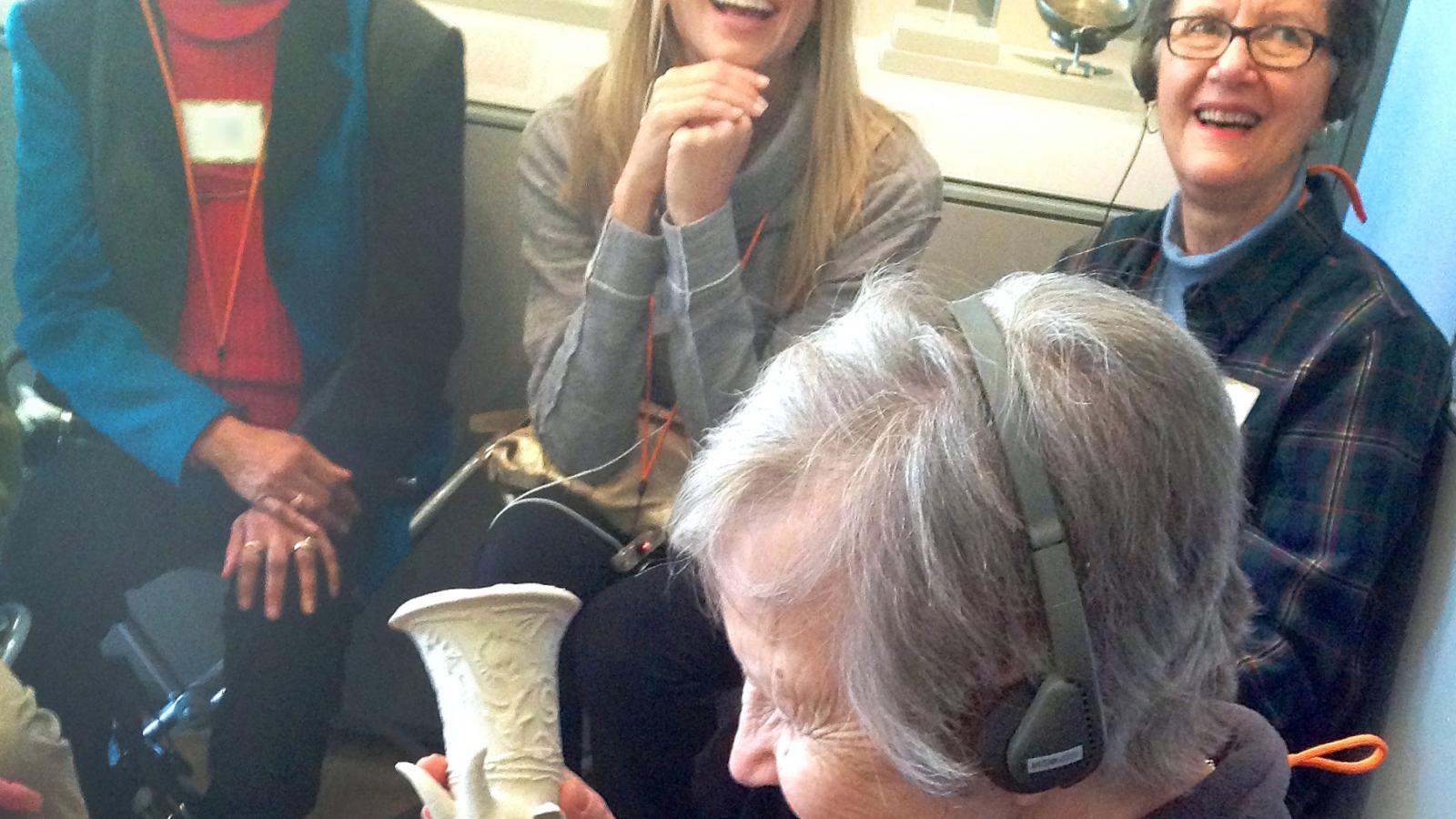 An older woman sits in a chair and holds a small sculpture. 