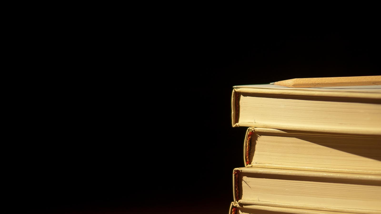 Four books stacked on top of each other. They are sitting on a empty table.