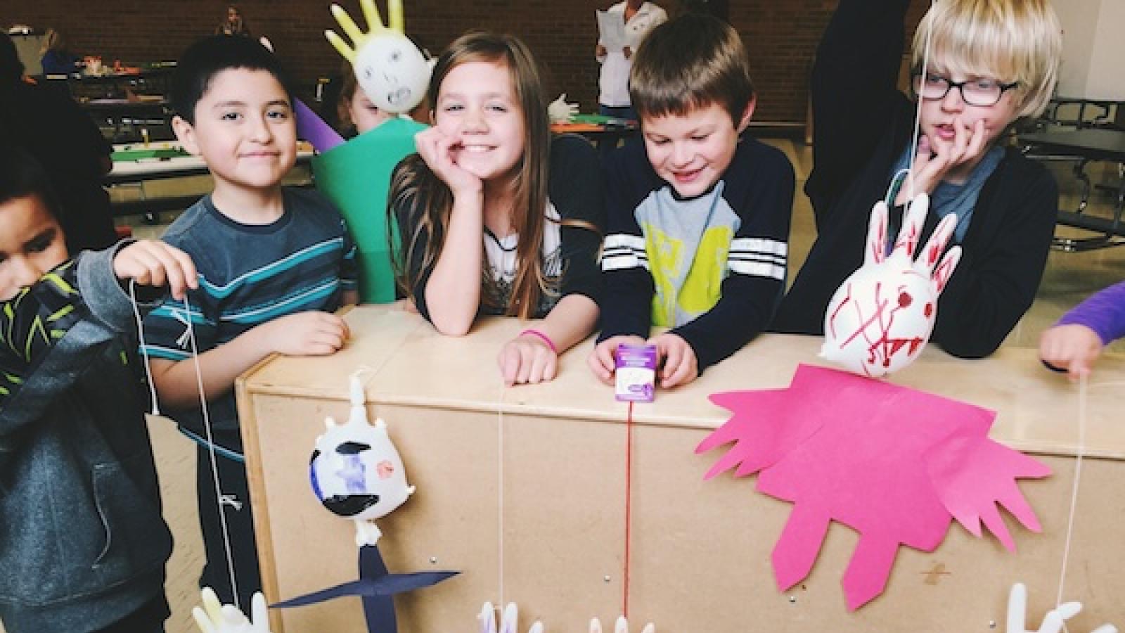 Several children pose with "people" made out of inflated latex gloves and paper
