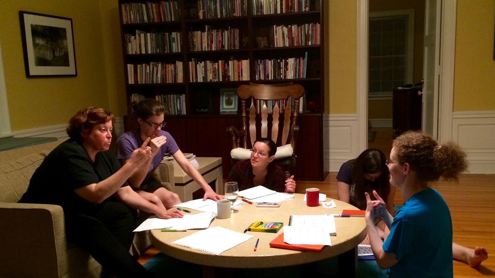 The five residents sitting around a coffee table communicating using ASL.