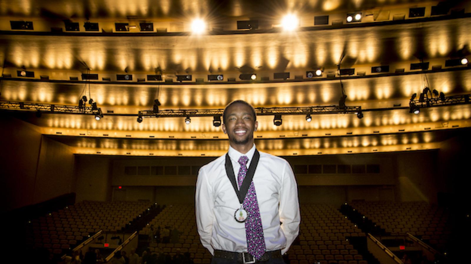 a young black man stands on a stage with back to audience and halo of stage lights