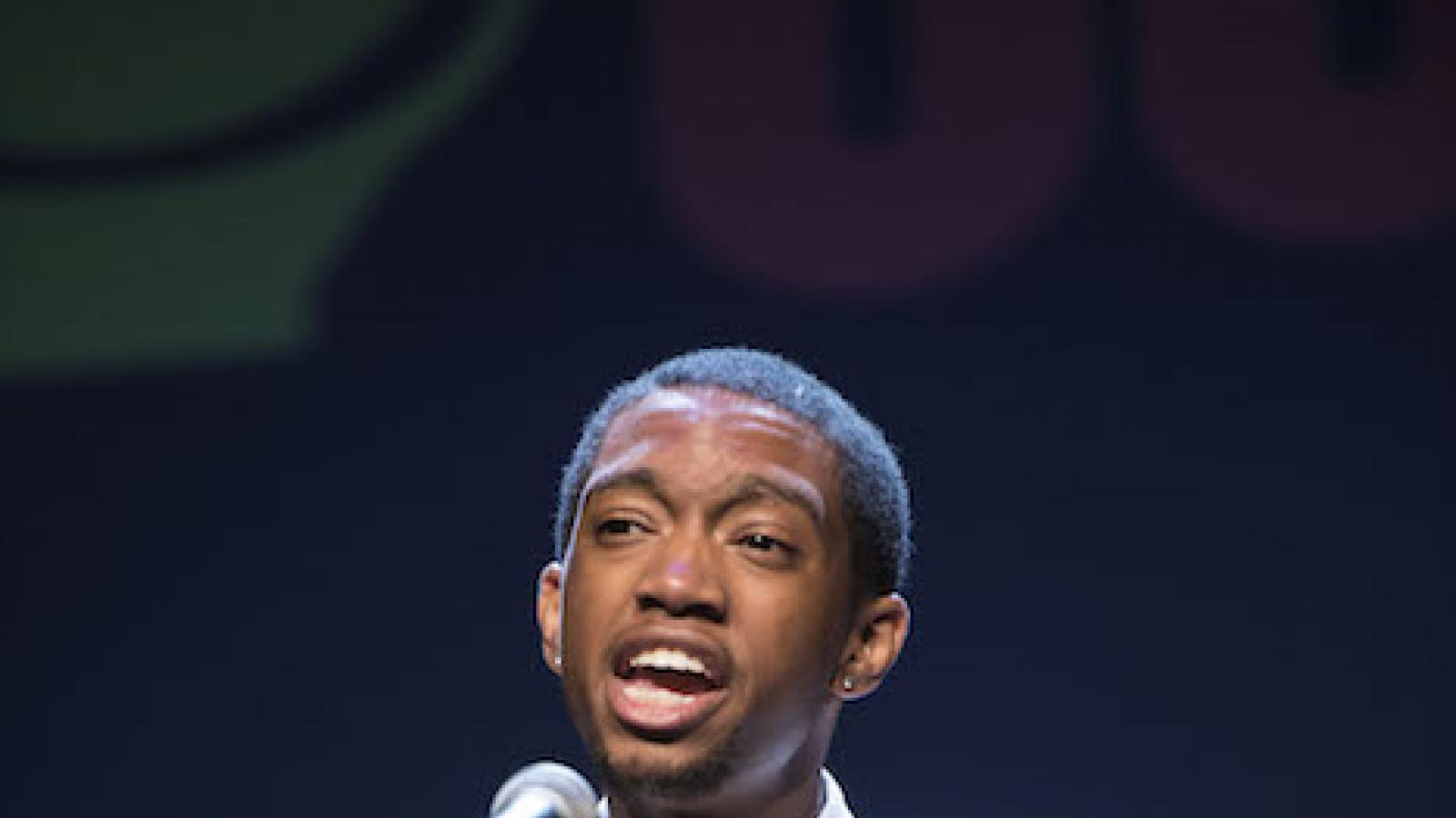 a young black man with short hair recites into a microphone