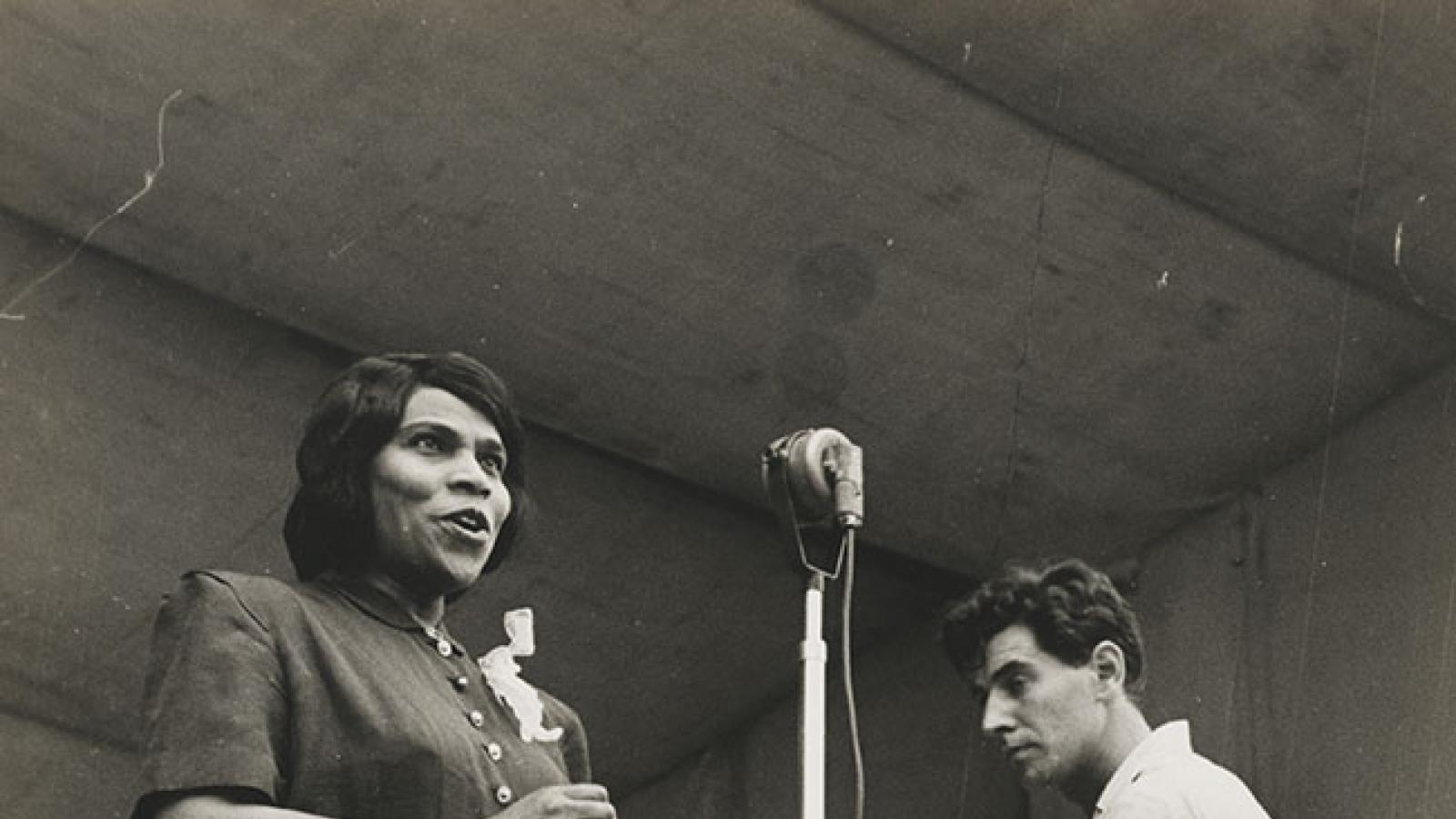 Marian Anderson and Leonard Bernstein A woman in 1940s dress sings before a microphone while a man behind her conducts unseen musicians