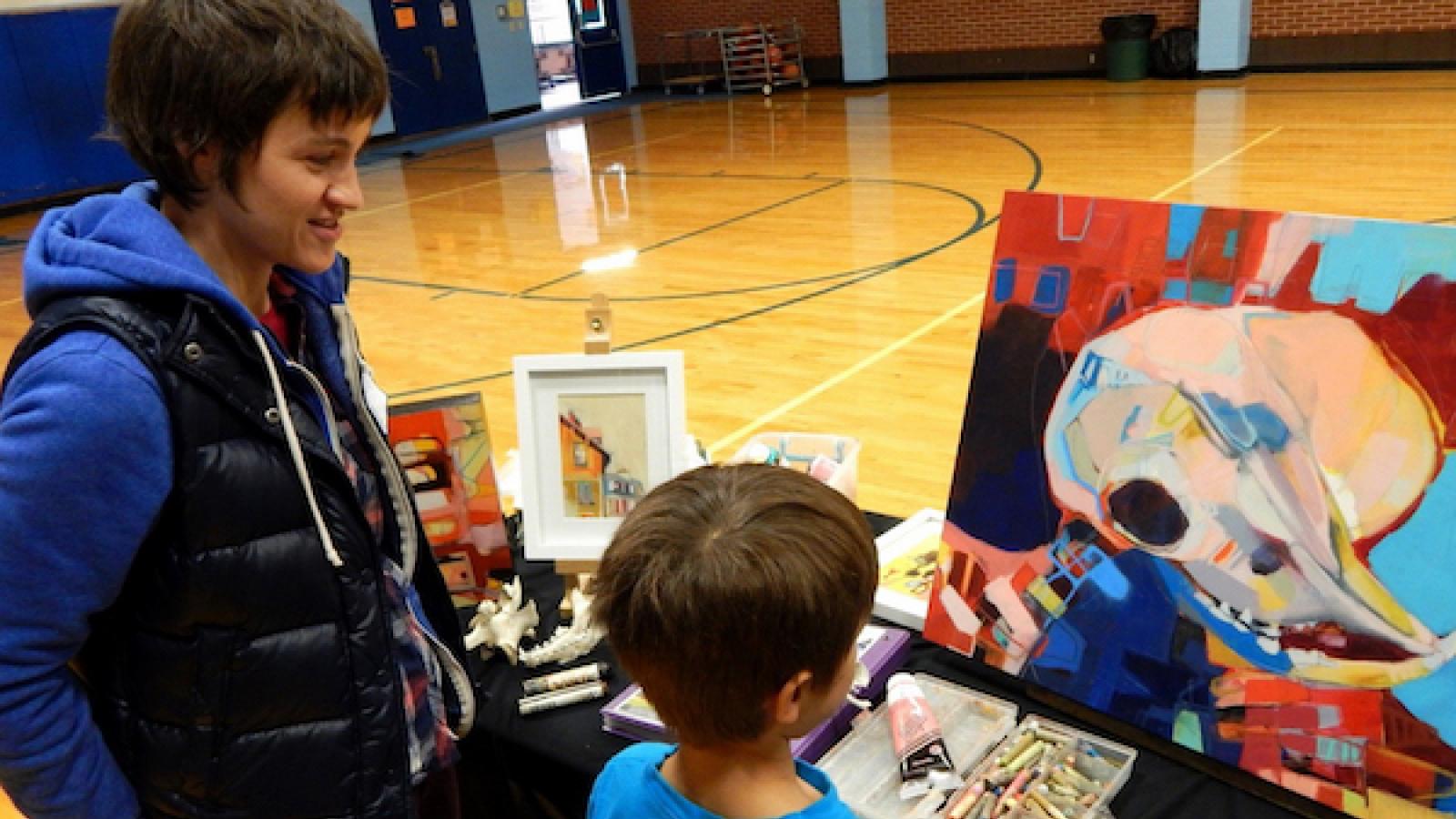 A woman artist talks to a young boy as he looks at one of her paintings provided by Art Mobile of Montana