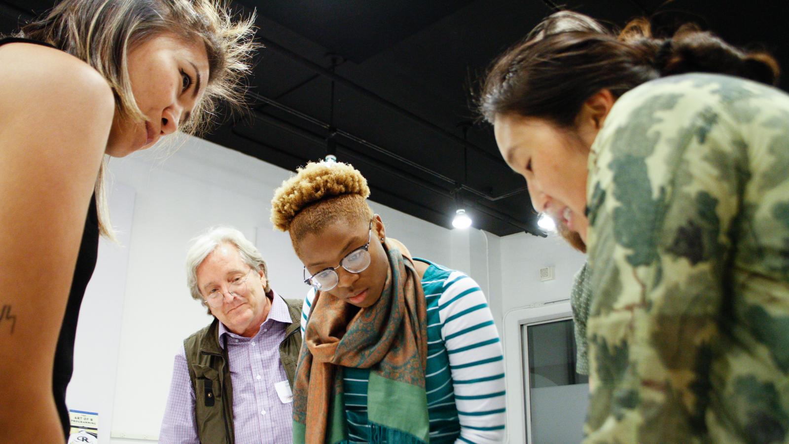 Three women and one men look down at a table