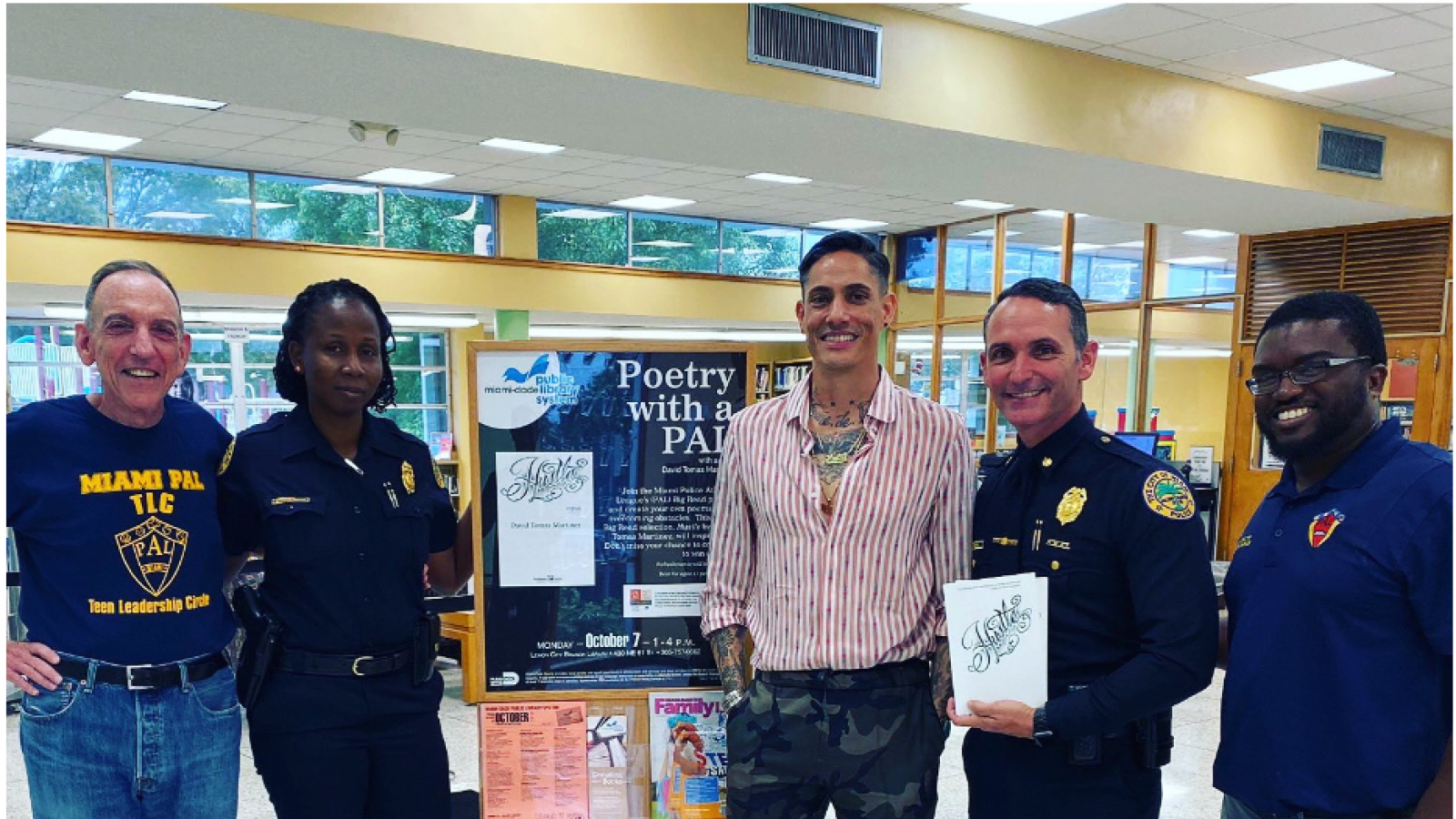 A group of men and women, some in police uniform, pose while smiling and holding a book