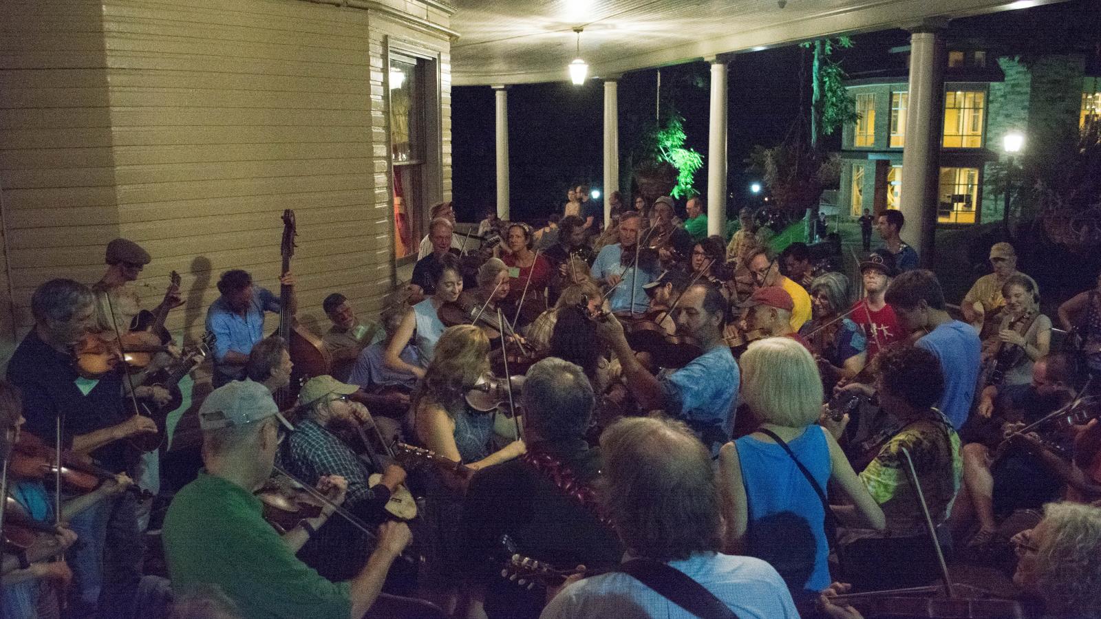 People pack together on a porch playing fiddles and basses