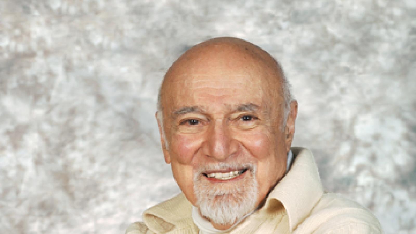 A man in a white sweater sits in a chair facing the camera