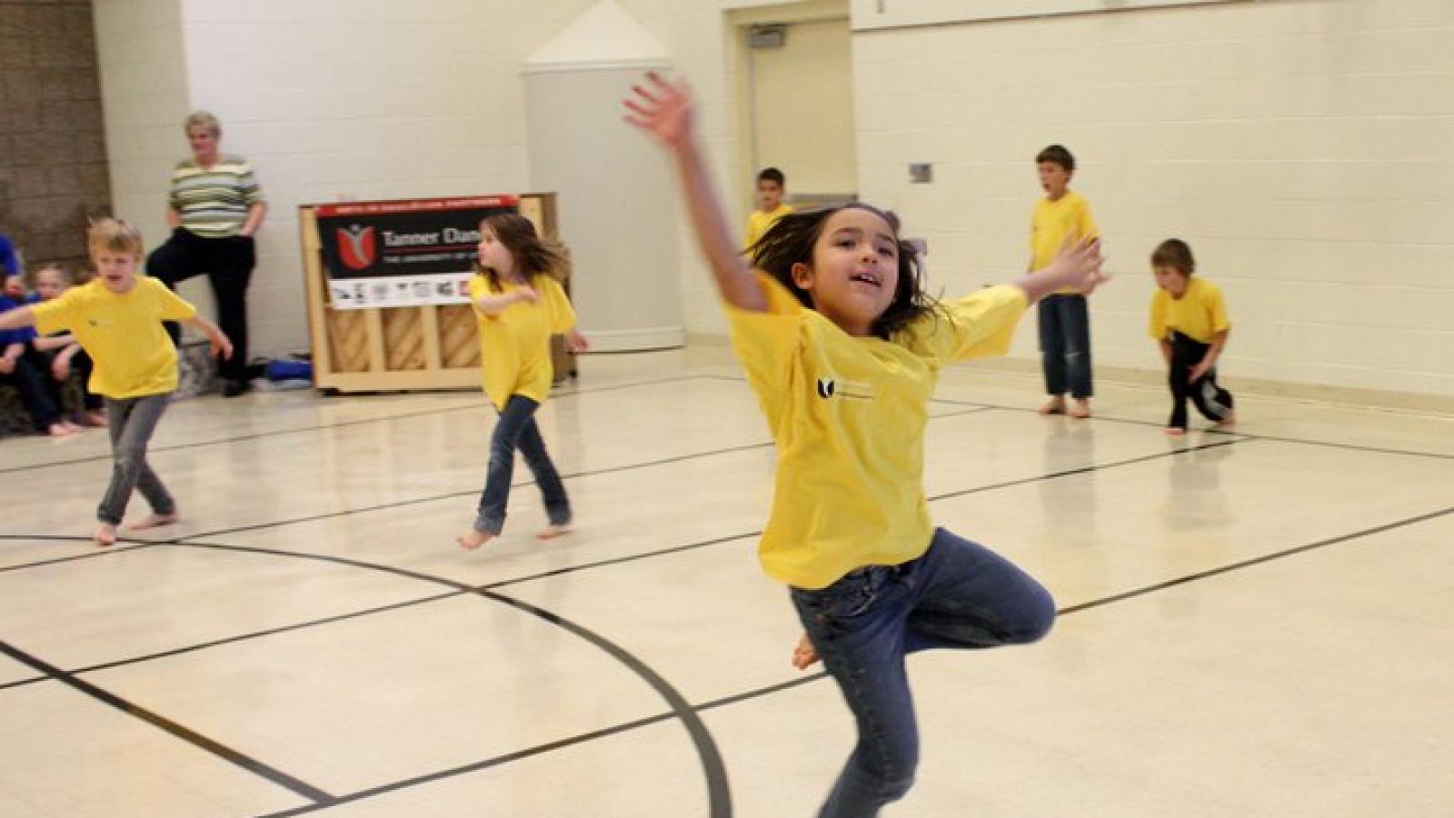 Children wearing t shirts dance in a school recreation room