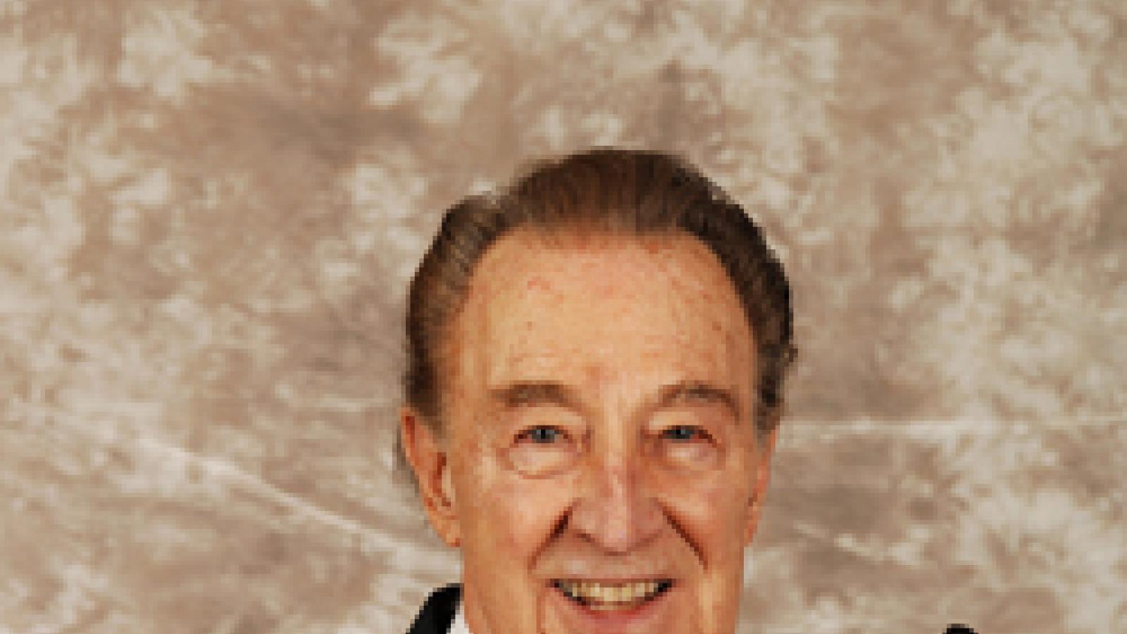 A man in a suit and tie smiles while holding a clarinet.