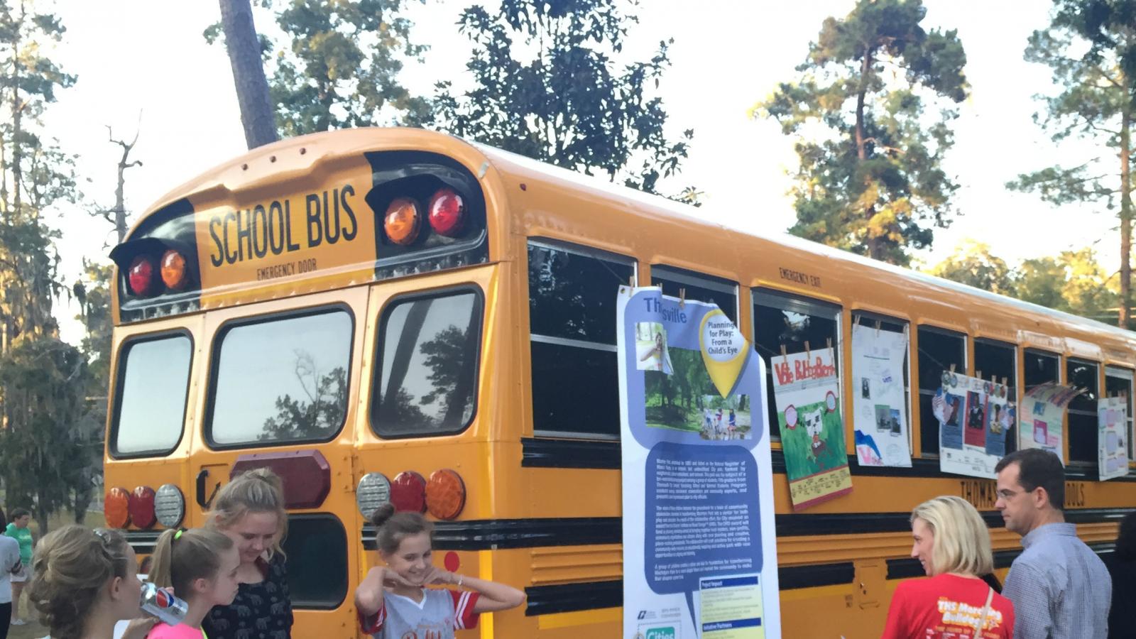 Teens at table next to school bus with posters on it.
