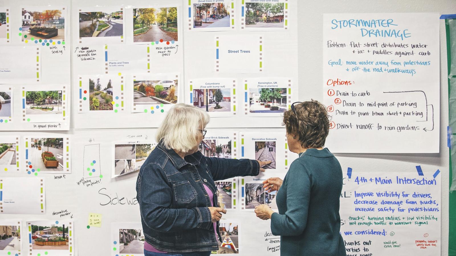 Two women standing in front of wall of pinned-up easel sheets