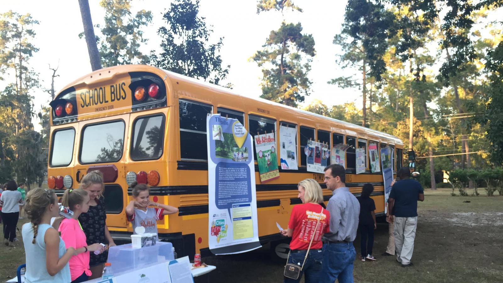 girls at a display next to a school bus with adults looking on