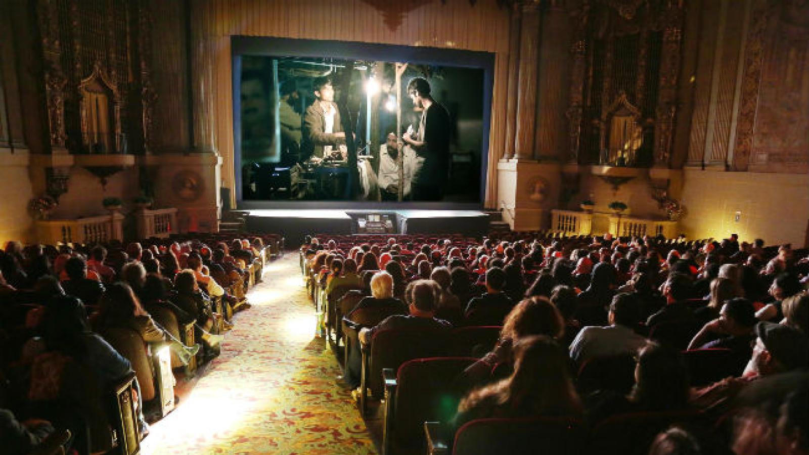 A movie plays on the screen of an ornate theater as an audience watches