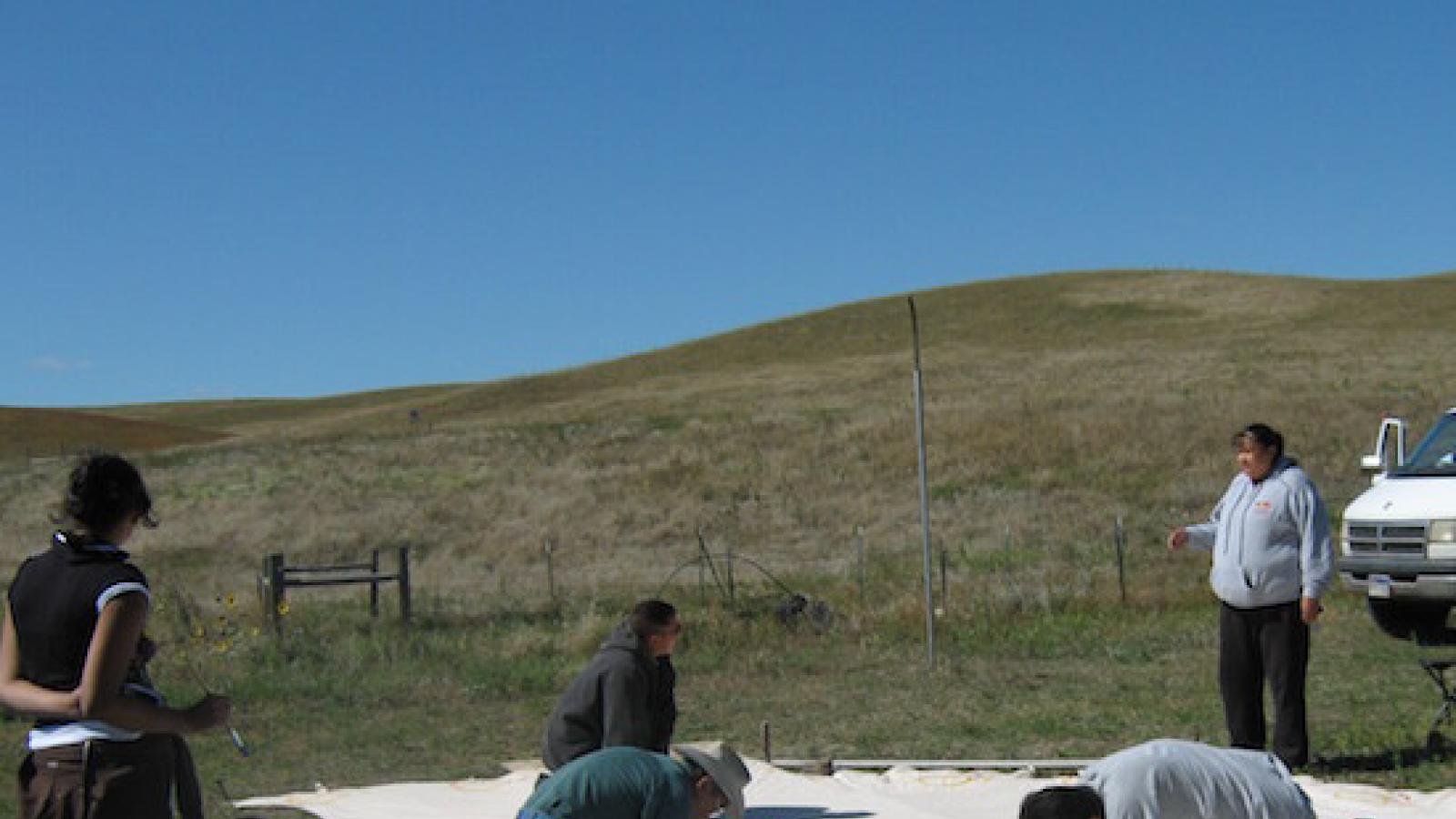 indigenous youth paint the walls of a tipi before it is assembled