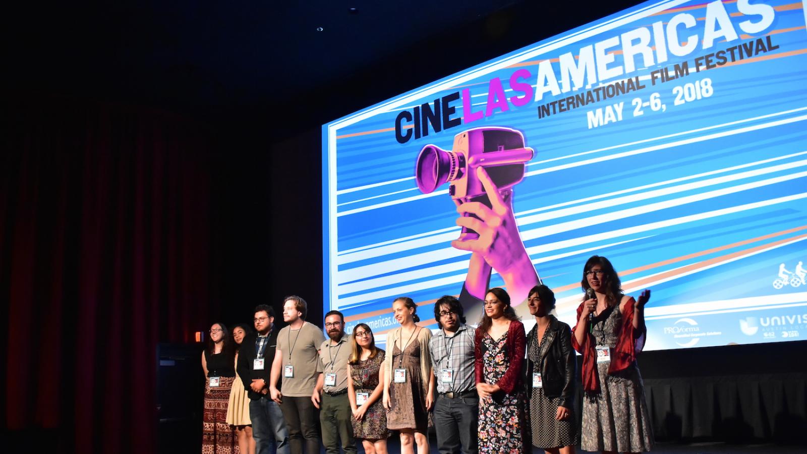 A group of people standing on a stage with a screen that says Cine Las Americas behind them