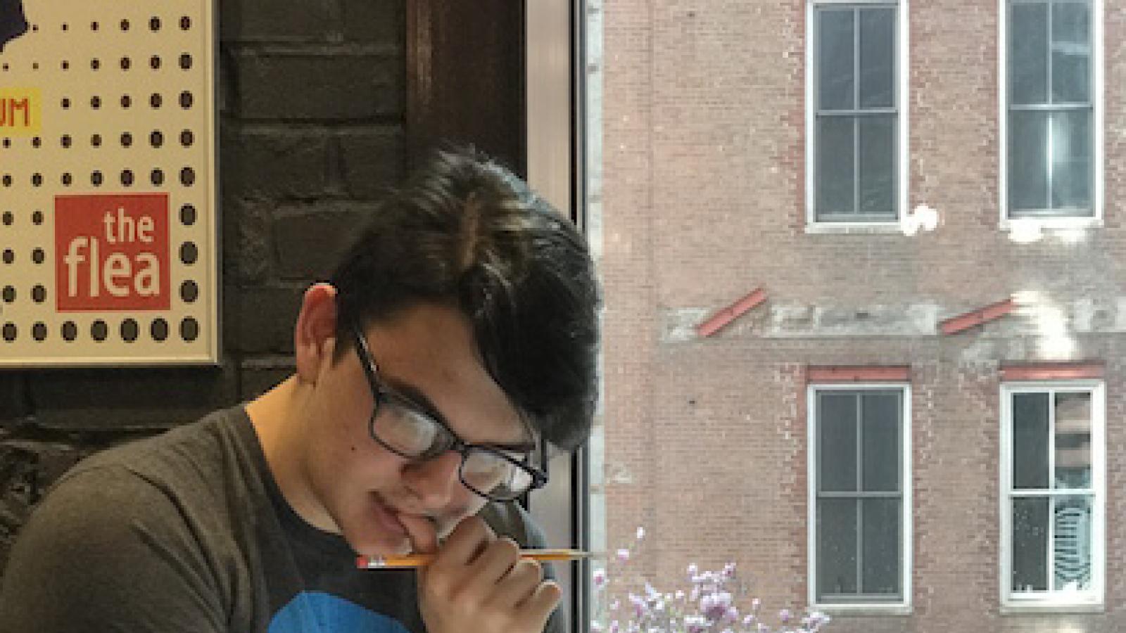  a young man sits in a chair near a window studying pages in a notebook