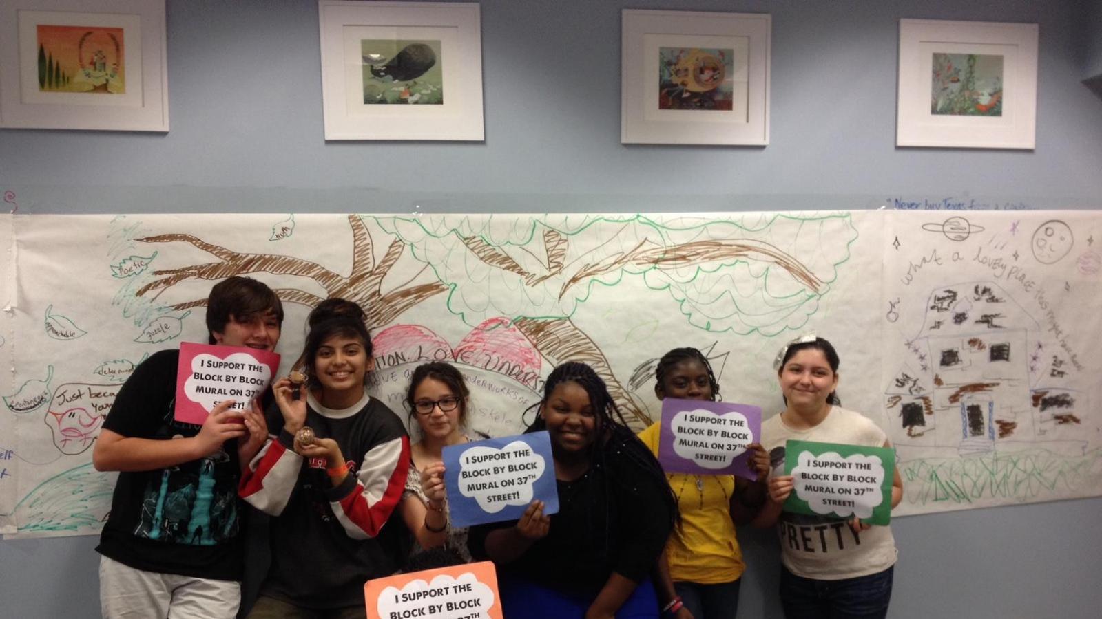 Children holding signs in front of a paper mural