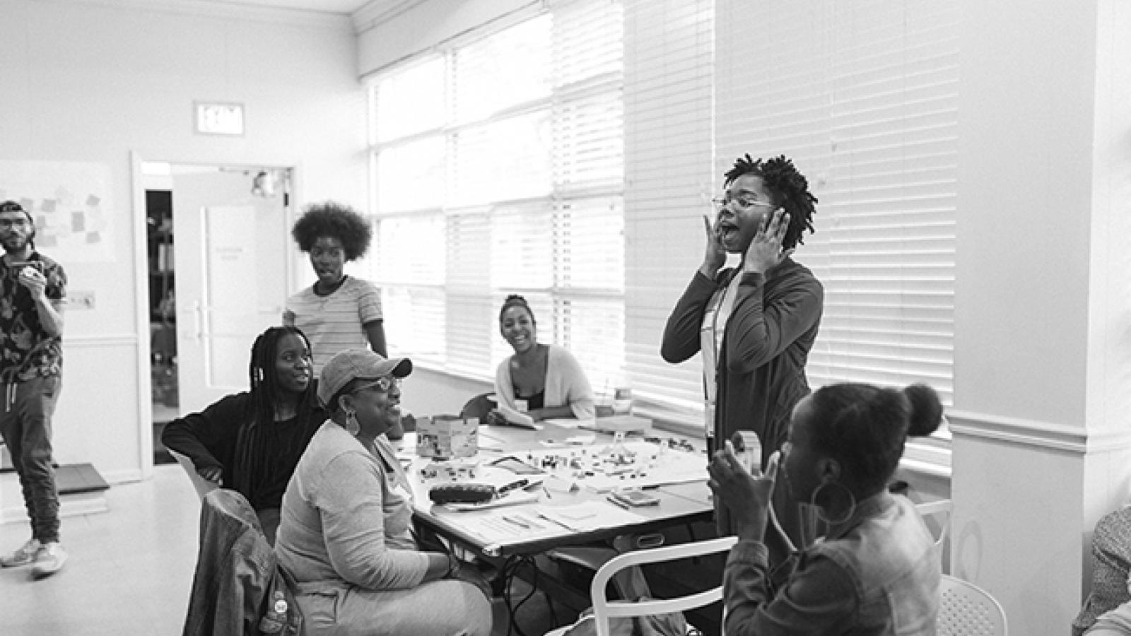 High school students sit around a table while one student stands and speaks