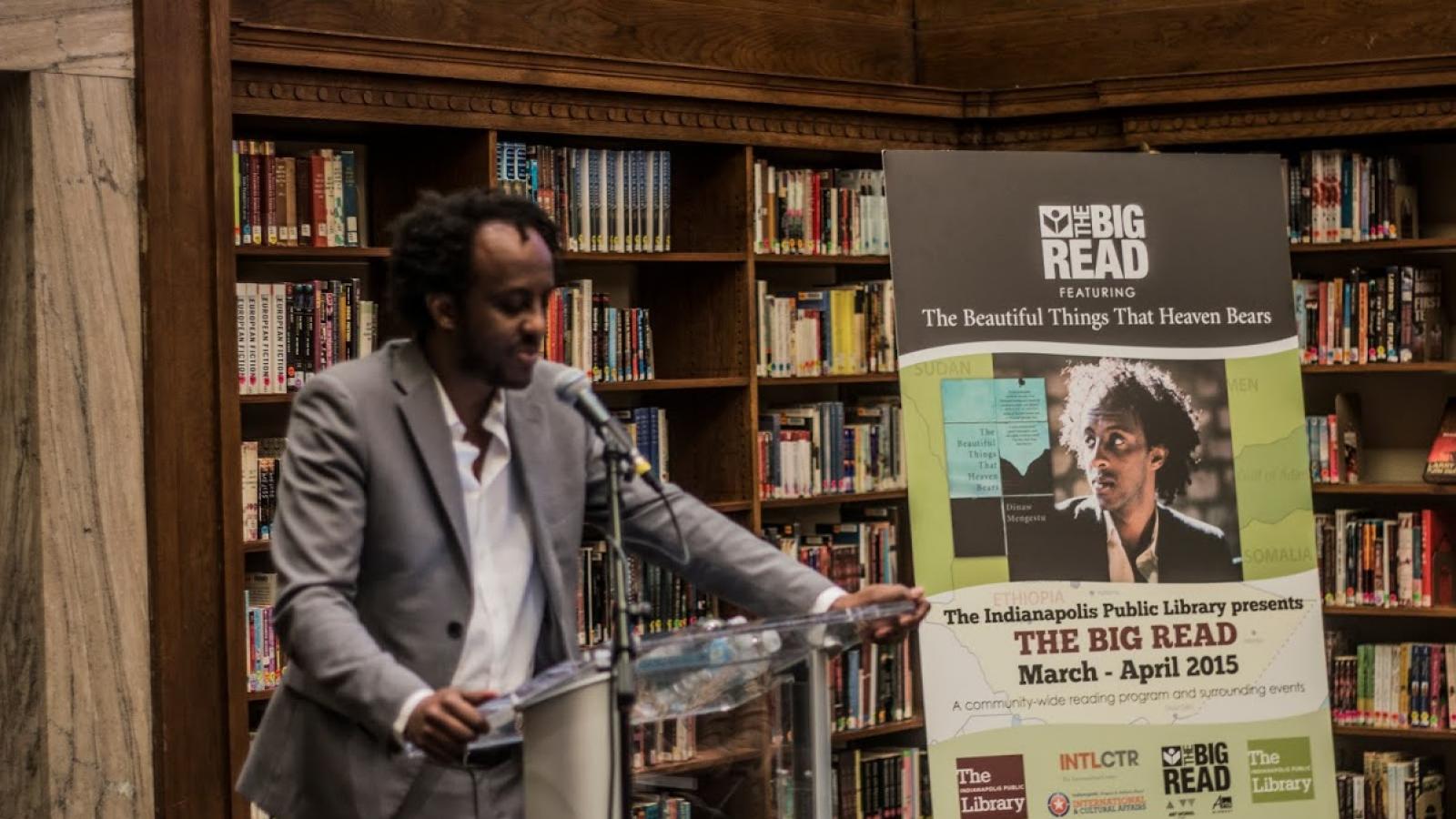 Author standing behind a podium speaking to a crowd of people. 