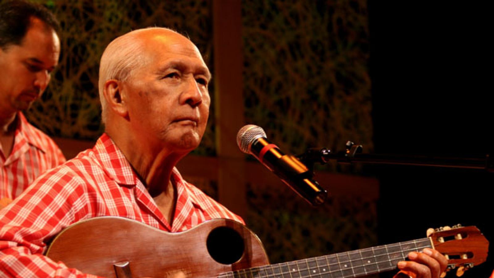A man in a red checkered shirt plays the guitar