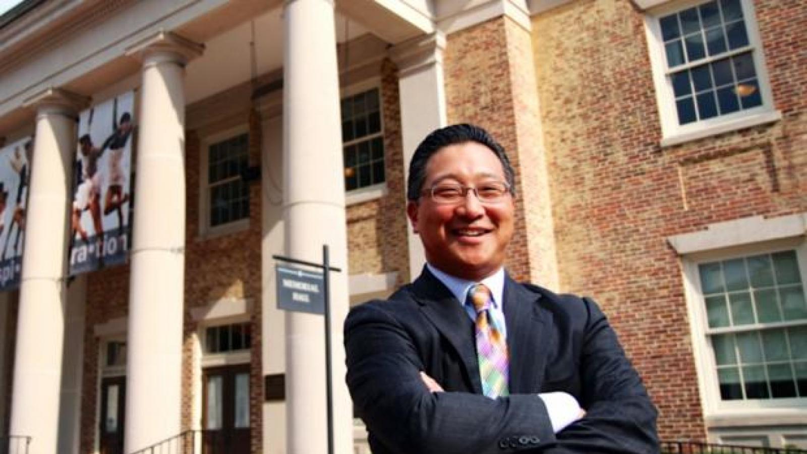 an Asian-American man with glasses posing out a college building