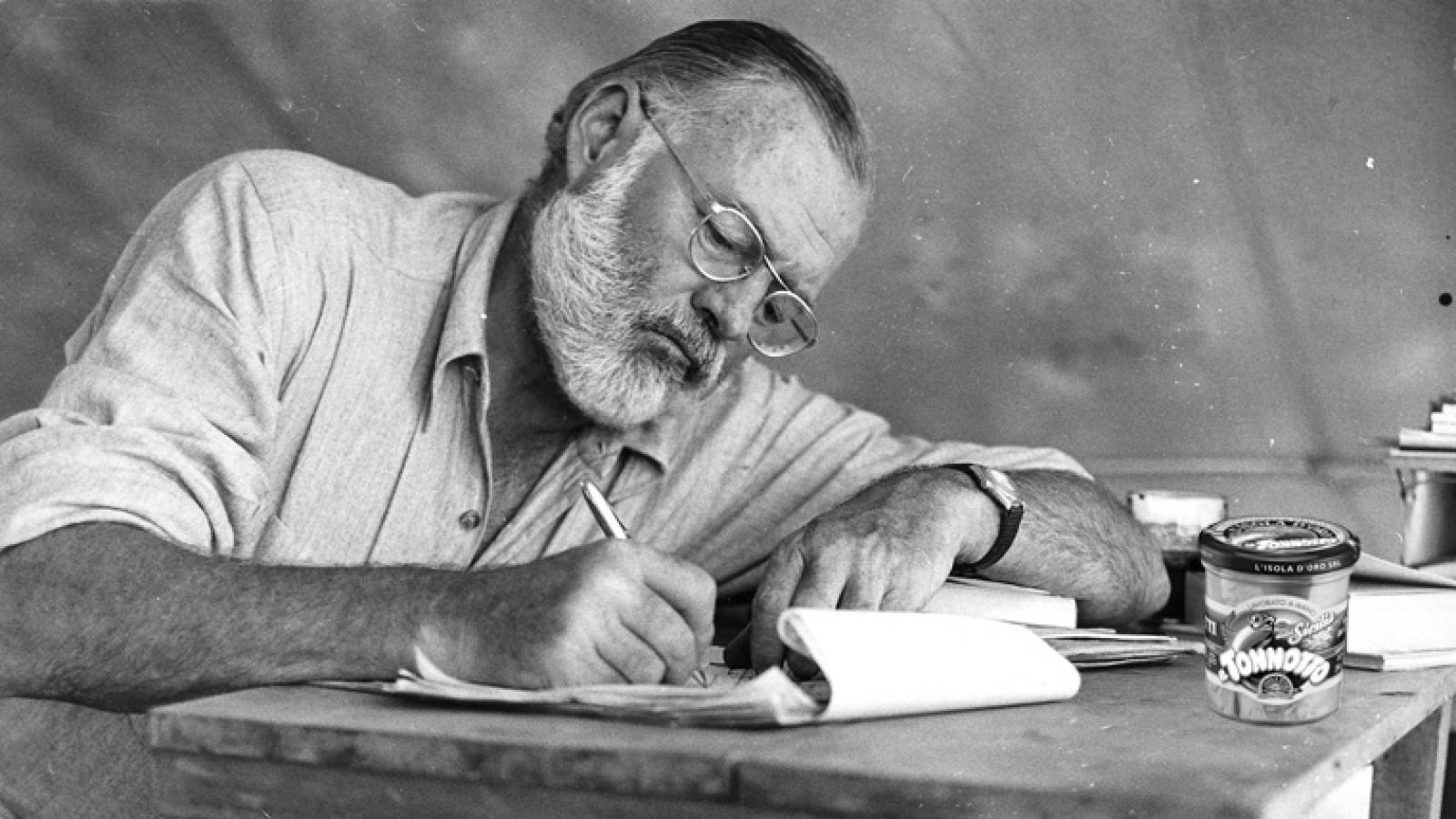 Ernest Hemingway sitting at a table and writing. 