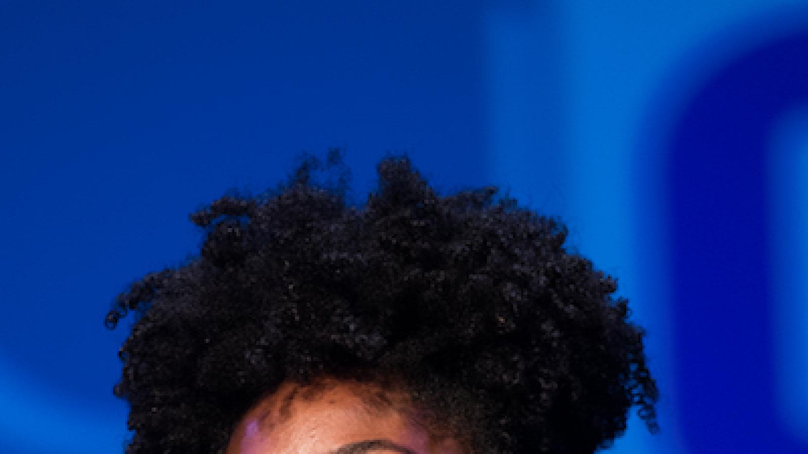 headshot of a young African American woman with her hair in an updo speaking into a microphone